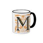 Oro y taza floral de "M" del negro -