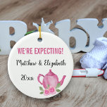 Adorno De Cerámica Esperamos que una niña pequeña esté preparando tet<br><div class="desc">Bonito adorno para su embarazo que usted puede personalizar. Un lado tiene flores rosas y tipografía escrita a mano con letras que dice "Una niña se está preparando". El otro lado tiene una linda tetera rosa y su texto personalizado. La plantilla está configurada para que edite la redacción de ejemplo...</div>
