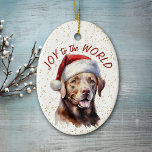 Adorno De Cerámica Labrador de chocolate recuperó alegría de perro al<br><div class="desc">En la parte delantera de este adorno navideño hay una hermosa imagen de un perro Labrador Recuperador marrón chocolate en un gorra de Santa Claus. Detrás de la imagen hay un fondo dorado que roce con tinta de color. El texto rojo dice "Alegría al mundo". La parte posterior del ornamento...</div>