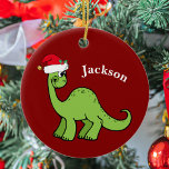 Adorno De Cerámica Navidades de los dinosaurios<br><div class="desc">Impresionante dinosaurio verde sonriendo y luciendo muy lindo en un festividad de sombrero rojo de Santa. Me gustan los animales de Navidades prehistóricos y los regalos que los niños amarán. Personalizar este regalo con el nombre del destinatario para hacerlo aún más personalizado.</div>