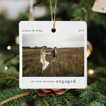 Adorno De Cerámica Nuestros primeros Navidades se comprometieron con<br><div class="desc">Un elegante árbol de navidad fotográfica adornado con la tipografía clásica "Nuestra primera navidad enganchada" en negro sobre un minimalista fondo blanco limpio. La foto, el texto, el nombre y el año se pueden personalizar fácilmente para que este ornamento sea único y personal para usted. ¡Un diseño de navidades simple,...</div>