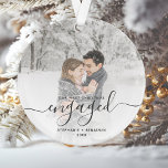 Adorno Foto personalizado First Christmas Engray Script<br><div class="desc">Conmemore su compromiso con este hermoso adorno de conservas moderno. El texto gris dice "Nuestra primera Navidad comprometida", con la palabra "comprometida" en un elegante guión de escritura a mano con flores antes y después. Reemplace la imagen de ejemplo con su foto favorita y agregue sus nombres y el año....</div>