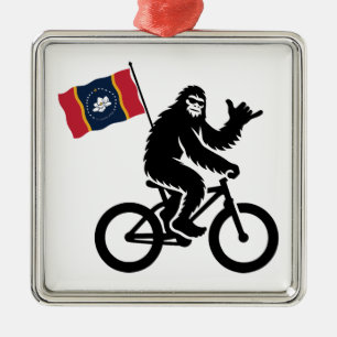 Adorno Metálico Bigfoot en bicicleta con la bandera de Mississippi