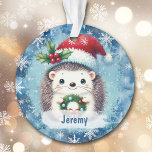 Adorno Nieto Cute Santa Hat Hedgehog<br><div class="desc">¡Aquí hay un adorable adorno de Navidad para ese nieto o nieta especial! Un pequeño erizo sostiene una corona y lleva un gorra de Santa Claus rojo y blanco decorado con bayas y bayas. La imagen se coloca sobre un fondo azul con copos de nieve blancos. El nombre de su...</div>