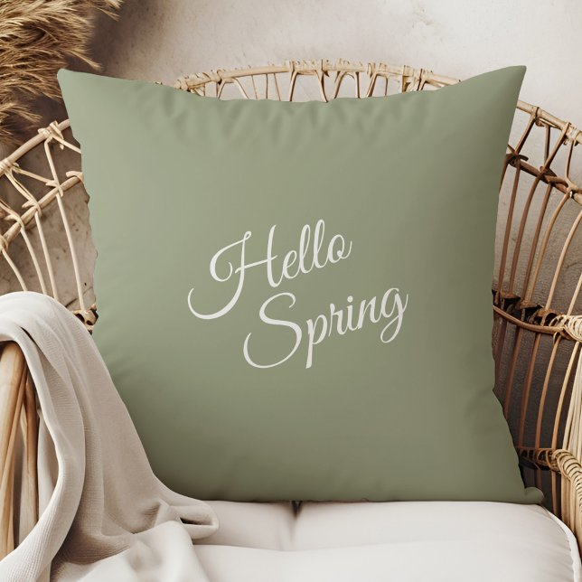 Almohada Verde Salvia Hola Primavera (Hello Spring Sage Green Throw Pillow in a  boho neutral rattan armchair.)