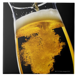 Azulejo Cerveza vertido en el vidrio, tiro del estudio