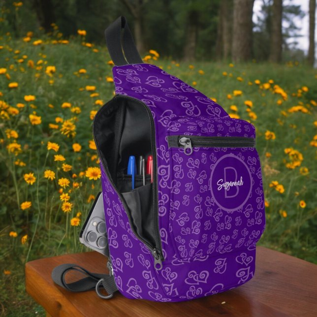 Bandolera Corazón vinculado sobre fondo morado y monograma (open side view of sling bag with linked heart pattern and monogram on front pocket)