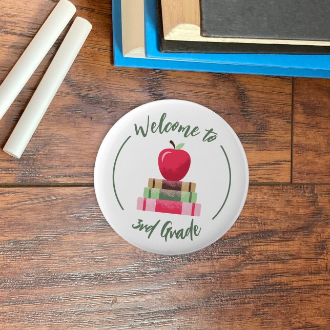 Bienvenido al botón de redondeo de los libros de A (Welcome to 3rd grade white round back-to-school button with a red apple and books .)