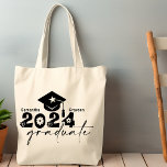 Bolso De Tela Graduado personalizado de 2024<br><div class="desc">La cita de Graduate Class de 2024 incluye una tapa con tassel,  topografía moderna y escritura caligráfica,  acentuada con flores y corazones. Fácilmente personalizable con su nombre de elección y monograma en la parte posterior. Gran idea de regalo para ese grado especial. (Color de la escuela: (negro)</div>