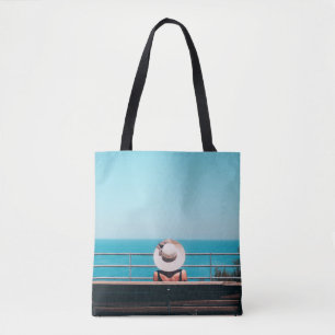 Bolso De Tela Mujer con gorra de paja blanca sentada en un banco
