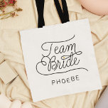 Bolso De Tela Nombre de Boda de oro de escritura moderna de Team<br><div class="desc">Este moderno bolso de tetas con un minimalista diseño de caligrafía de escritura de moda casual leyendo TEAM BRIDE, así como el nombre personalizado de su dama de honor o dama de honor, cuenta con líneas limpias para crear un aspecto elegante y sofisticado. El estilo sobrio, con detalles de corazón...</div>