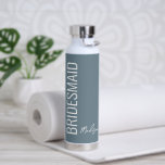 Botella De Agua Bridesmaid Dusty Blue White Script personalizado<br><div class="desc">Sorprenda a sus bodas chicas con este frasco de agua con guijarros blancos y polvos de Bridesmaid. Se trata de un minimalista moderno con un fondo azul personalizable. El texto es "dama de honor" con letras blancas grandes verticales en la parte delantera izquierda. El nombre está en la línea de...</div>