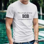 Camiseta Es duro ser Bob<br><div class="desc">Camiseta graciosa dice en letras negras,  "Es un trabajo duro ser BOB pero alguien tiene que hacerlo". Personalizar con tu propio nombre o hasta personalizarlo cambiando las palabras. ¡Hace un gran regalo! ¡Adelante,  ponle una SONRISA en la cara!</div>