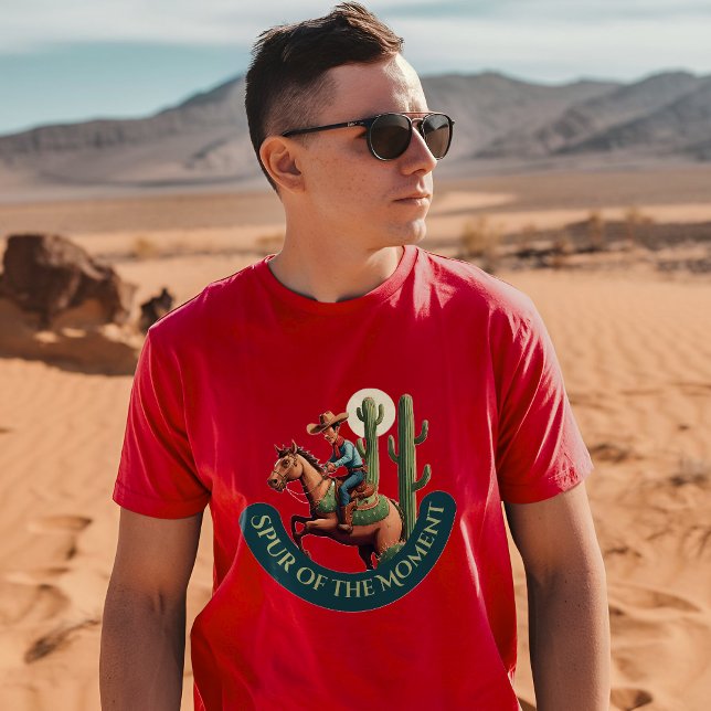 Camiseta Goma del momento gráfico de Cowboy (A man wearing a cardinal t-shirt with a cowboy and cactus design stands in a desert landscape)