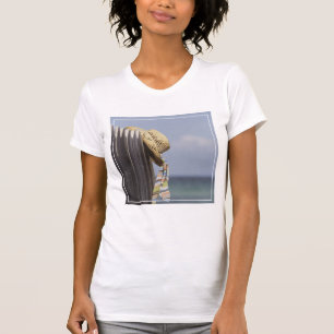 Camiseta Gorra de paja que cuelga en la cerca en la playa