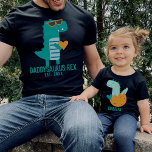 Camiseta Guay Dino Daddysaurus Rex Día del Padre Nuevo<br><div class="desc">Diseño de texto de personalizable con una moderna y fresca T-rex verde azulada en gafas de sol sosteniendo un corazón,  regalo para el día del padre,  cumpleaños o Navidades. Encuentra una camiseta de dinosaurio infantil en mi colección "diseños de papi y yo".</div>