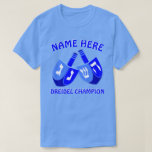 Camiseta Jánuca Dreidels en el campeón lindo azul de<br><div class="desc">Añada un nombre a esta camiseta divertida de Jánuca del campeón de Dreidel para un regalo personalizado o como poca invitación para sí mismo. El diseño gráfico intrépido de los dos Dreidels en sombras brillantes de azul y del blanco incluye una plantilla para su nombre arriba con el "campeón de...</div>