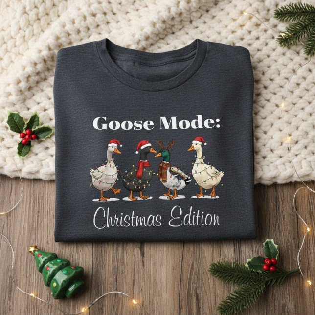 Camiseta Triblenda Goose Mode Christmas Edition T-Shirt (folded dark gray Christmas shirt with goose design on cozy knit blanket and festive decor)