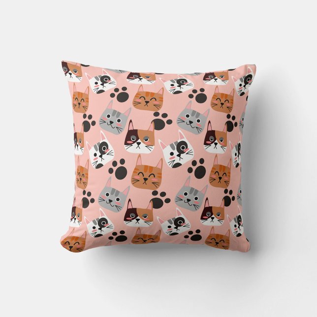 Cojín Decorativo Caras de gato (A flat lay shot shows a square pillow with a pink background and a repeating pattern of cartoon cat.)