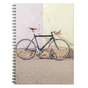 CUADERNO BICICLETA NEGRA Y GRIS EN MURO BLANCO