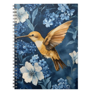 Cuaderno colibrí dorado volando entre flores azules y blanc