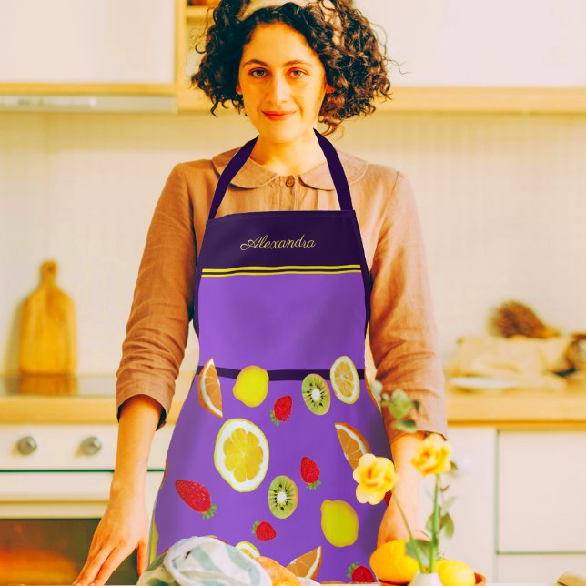 Delantal Frutas de verano frescas personalizables (A woman in a kitchen wearing a beautiful purple apron decorated with lemons, kiwis, strawberries)