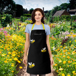 Delantal Moda de monograma negro de abejas amarillas<br><div class="desc">Un elegante fondo negro. Decorada con abejas sonrientes y alegres. Personalice y agregue su nombre, escrito con un estilo de escritura a mano blanca con letras a la moda y con toques. Para que los cambios sólo eliminen el nombre del ejemplo, deje los espacios o la emoji delante y después...</div>