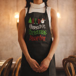 Delantal Navidades obsesivos desordenan festividades gracio<br><div class="desc">OCD. Navidades obsesivos desordenan el delantal de negro con escritura verde,  roja y blanca. Un gracioso regalo de Navidades con un lindo árbol de navidad y Santa Claus para decorar las palabras. Regalo de humor navideño.</div>