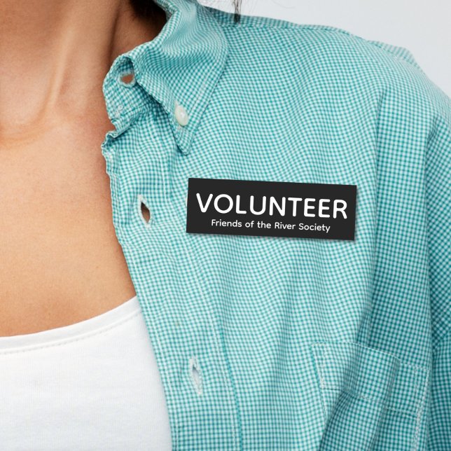 Etiqueta de nombre de placa de voluntario clásico  (Woman in blue shirt wearing this customizable volunteer name tag badge with white letters on black.)