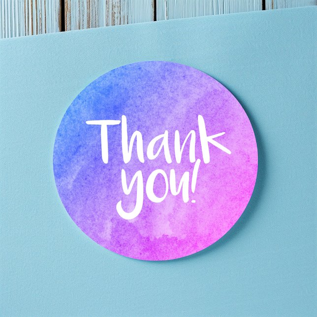 Gracias pegatina brillante acuarela (Round thank-you sticker with a blue and purple watercolor gradient and handwritten-style white text.)