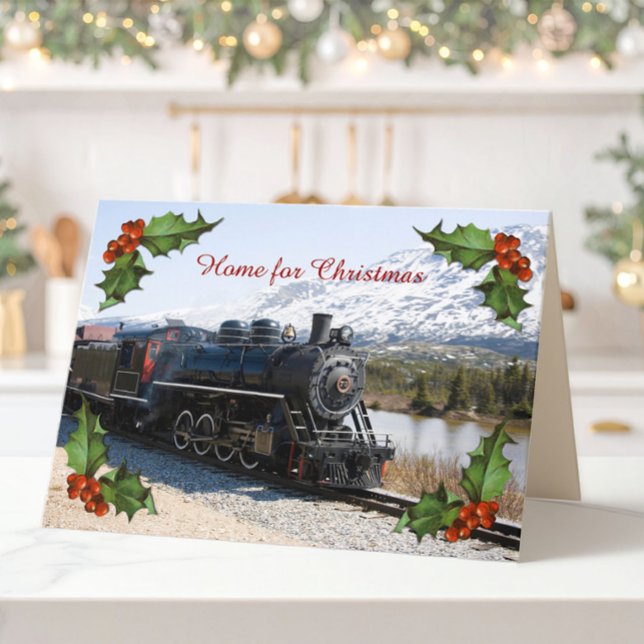 Hogar en la tarjeta del tren para Navidades (A folded Christmas card of an old steam train, snowy mountains and corner decorations of holly.)
