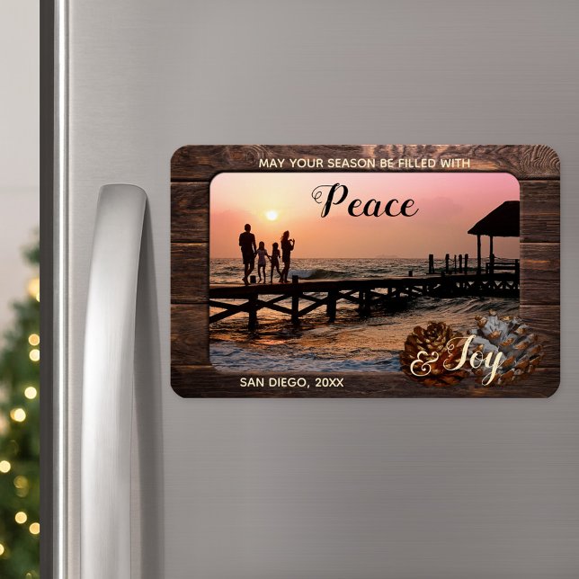 Imán de fotos navideñas personalizadas de madera r (A Christmas magnet featuring your custom photo framed by rustic dark wood and festive pine cone)