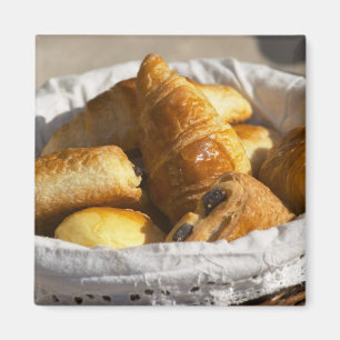 Imán Una cesta de desayuno de mimbre con cruasanes, y