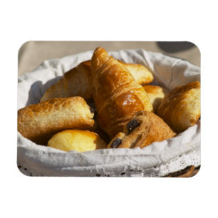 Imán Una cesta de mimbre para desayuno con croissants,