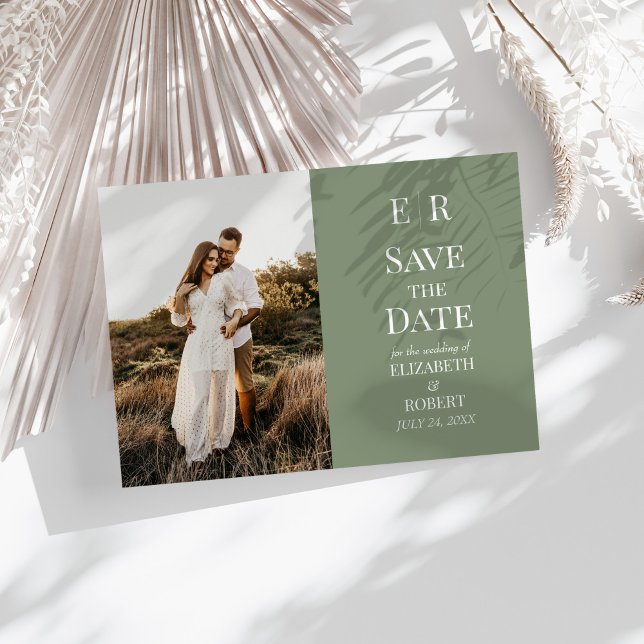 Invitación Foto de un monograma de oliva moderna Guardar la t (Modern Olive Monogram Photo Save the Date Card on a sunny white table with neutral dry botanicals.)