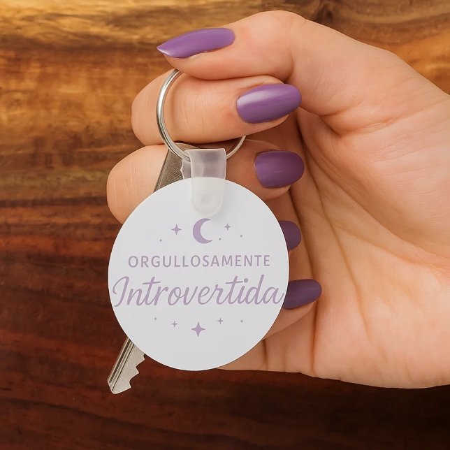 Llavero redondo “Orgullosamente introvertida”  (Una mano de mujer con sus uñas pintadas de morado cogiendo unas llaves con su llavero favorito.)