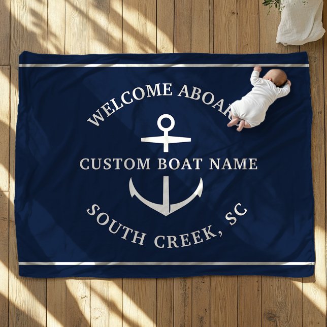 Manta Polar Nombre de barco Personalizado moderno bienvenido a (A baby, dressed in white, lies on a navy blue blanket with an anchor motif. Text is Welcome Aboard")