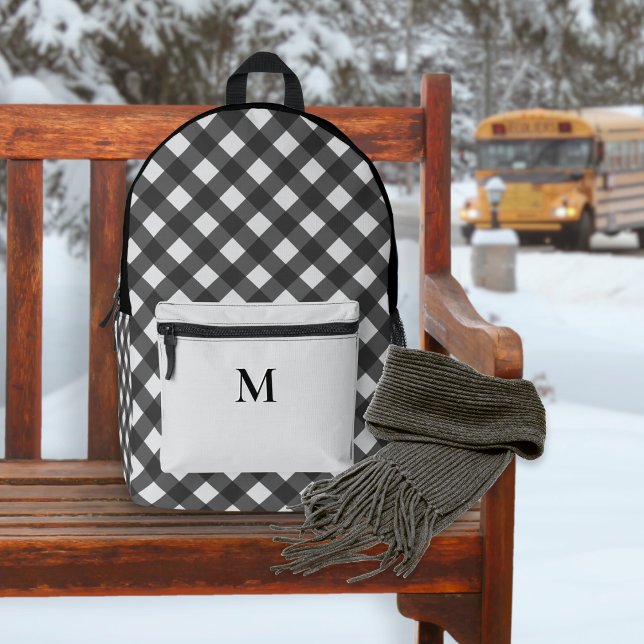 Mochila Impresa Monogramado de patrón negro y gris con relleno de  (A backpack with black and white buffalo check pattern and monogrammed silver-gray front pocket)