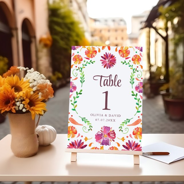 Número de mesa de boda Fiesta Floral Mexicana Blan (White Mexican Floral Fiesta Wedding Table Number on a table with flowers.)