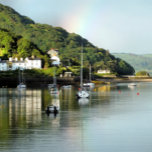 PAÑO DE COCINA VISTAS DE GALES<br><div class="desc">Después de un día de lluvia, finalmente sale el sol y aparece un arco iris en el cielo, en este hermoso paisaje del puerto de Aberdyfi en Gales, con botes en el agua y algunas de las casas de la aldea.</div>