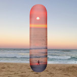 Pasear por el Golden Naranja Sunset Skateboard<br><div class="desc">Este skateboard muestra una imagen de una persona caminando a través de los rayos rosa dorados y naranjas de la puesta de sol. Los rayos de color crean un orbo que silueta al caminante.</div>