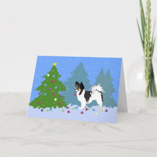 Perro Papillon decorando árbol de Navidad en bosqu
