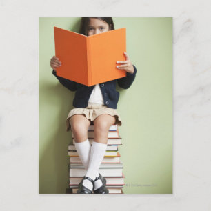 Postal Chica de raza mixta sentada en una pila de libros