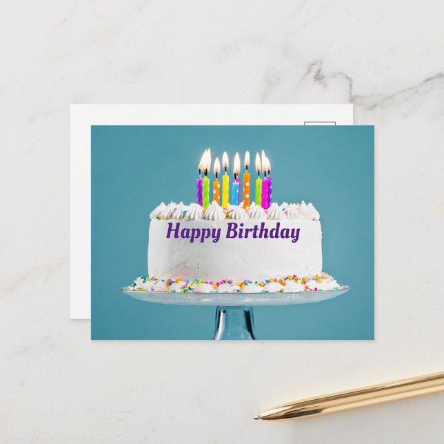 Postal feliz cumpleaños para pasteles (A beautifully decorated birthday cake with colorful candles lit on top, set against a soft blue back)