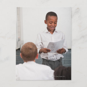 Postal Niño parado frente a la lectura de clase en 2
