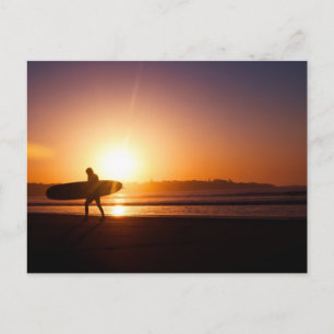 Postal Surfista llevando Surfboard en la playa al atardec