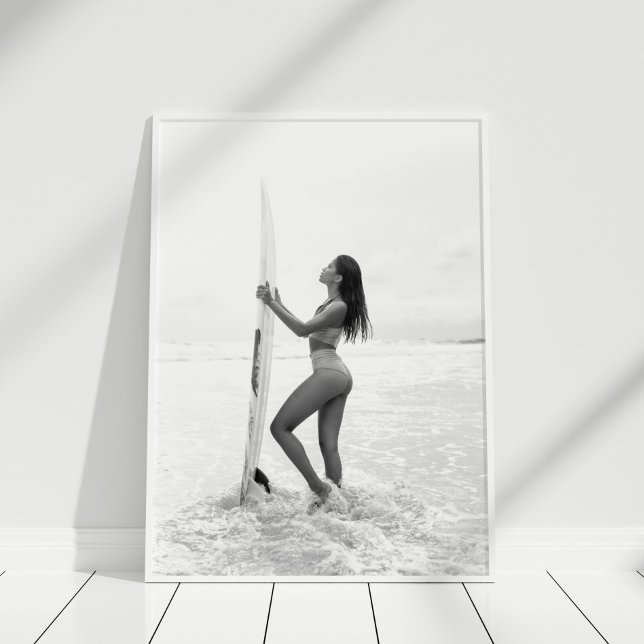 Póster Chica de los surfistas blancos y negros en la play (Black and White Surfer Girl on the Beach Poster in white frame on wooden floor.)