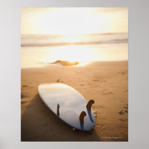 Póster Surfboard laying on beach at sunset