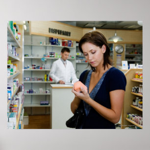 Póster Young woman looking at medicine in pharmacy,