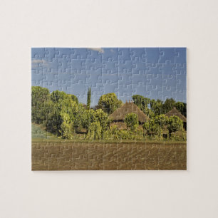 Puzzle Un campo cultivado frente a casas con techo de paj